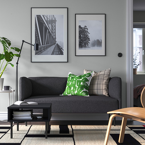 Sofá LILLEHEM gris con almohadas verdes, mesa de centro negra y plantas.