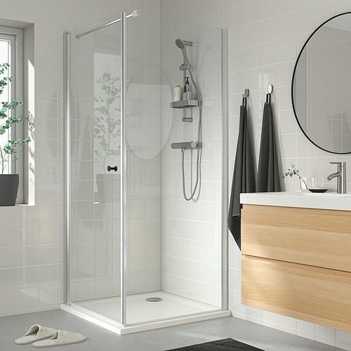 Baño moderno con ducha de vidrio, accesorios de plata, toallas para colgar, espejo redondo y planta. Cabezal de ducha: VALLAMOSSE, cromado, ajustable, se adapta a la pared.