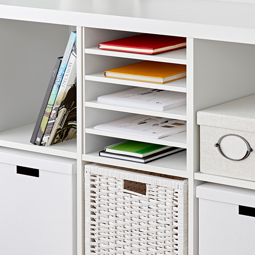 Estantería KALLAX blanca con cuatro separadores verticales, que sostienen libros de colores y una cesta de mimbre.