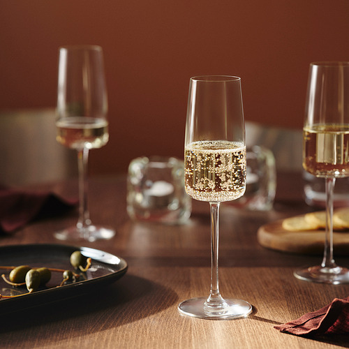 Tres copas de champán sobre una mesa de madera, una con vino espumoso, rodeadas de entremeses y platos.