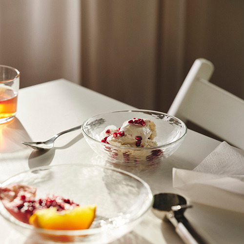 Tazón de helado con semillas de granada sobre la mesa con vaso y fruta, mostrando un diseño elegante.
