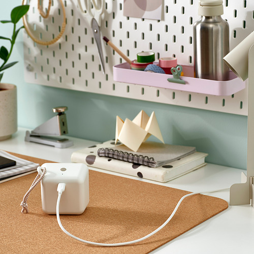 Un escritorio con un cable usb-c blanco, cuadernos, origami y una planta. El cable es flexible y conecta dispositivos.