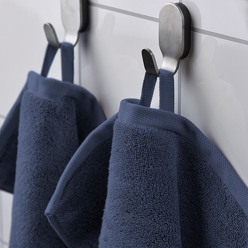 Dos toallas azules cuelgan cuidadosamente de ganchos metálicos contra una pared ligera. Las toallas cuentan con una superficie texturizada y absorbente y un borde tejido.