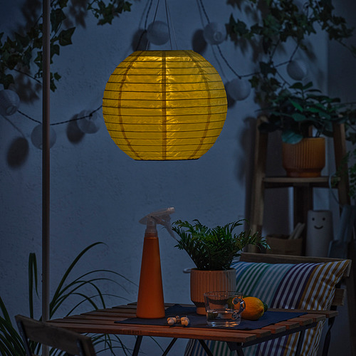 Patio nocturno con linterna solar, regadera, planta, vidrio, naranja.