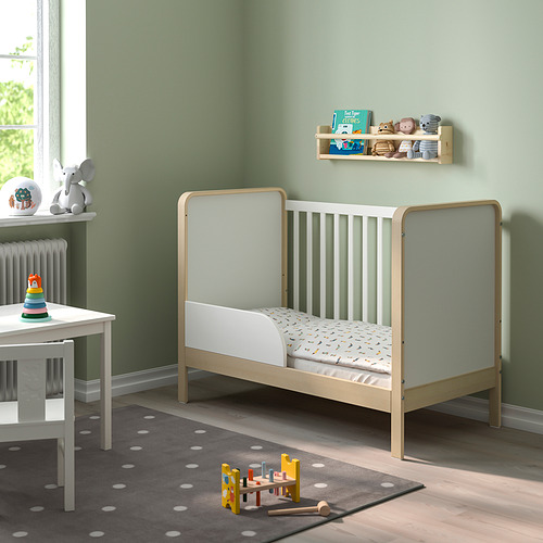 Guardería moderna con cama para niños pequeños ÄLSKVÄRD de madera clara, alfombra blanca, apilador de juguetes y estantería que crea un espacio acogedor.