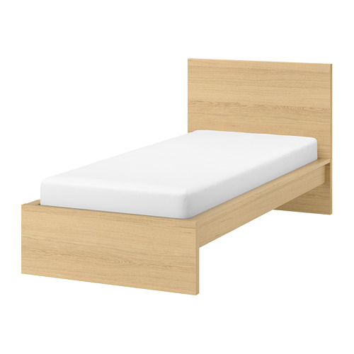 Cama minimalista de madera clara con colchón blanco, cabecero alto, líneas limpias.