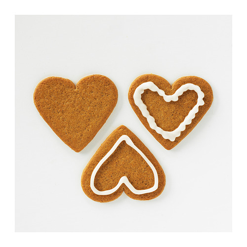 Tres galletas en forma de corazón, de color marrón con glaseado blanco alrededor de los bordes sobre una superficie blanca.