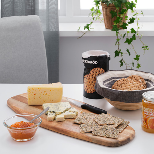 Tabla de cortar de madera con queso, galletas saladas, cuchillo y mermelada en la mesa del comedor, utilizada para servir la comida.