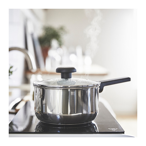 Cocina moderna con cacerola MIDDAGSMAT en la estufa. Plateado, redondeado con asa y tapa negras. Cocción sobre quemador eléctrico.
