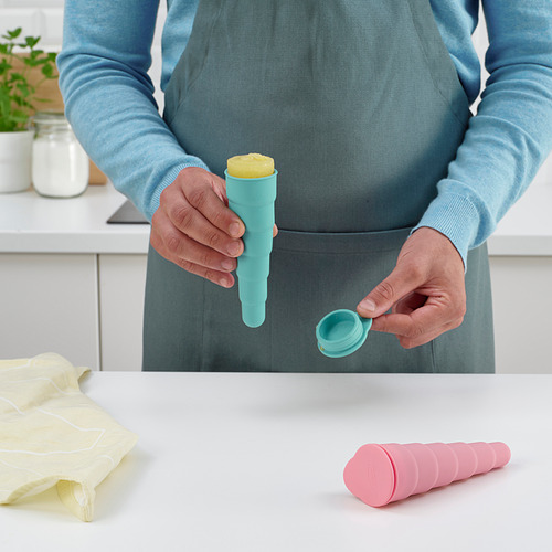 Persona sosteniendo un molde de paleta helada, demostrando cómo ensamblarlo. Otros moldes en la encimera de la cocina, junto con el paño y el frasco.