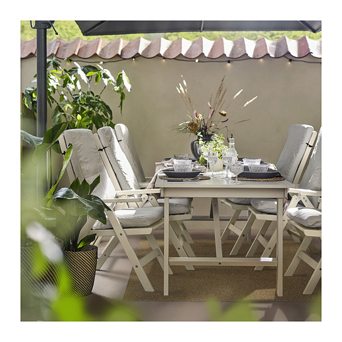 Patio exterior con alfombra LÄTTBETONG beige y marrón, mesa, sillas y plantas blancas.