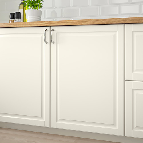 Gabinetes de cocina blancos con paneles biselados, con encimera de madera, manijas plateadas y una planta verde.