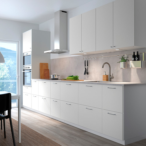 Modernos armarios de cocina blancos VALLSTENA con superficies elegantes, altos con cajones y puertas, electrodomésticos de acero inoxidable, habitación luminosa con gran ventanal.