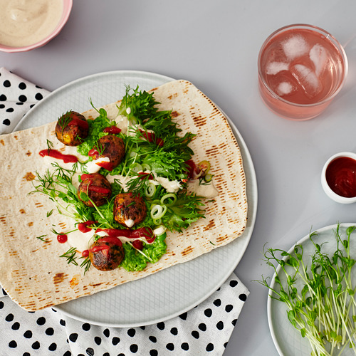 Wrap de pan plano con ensalada verde, salsa y carne en plato blanco con bebida.