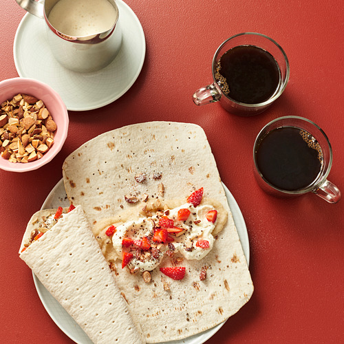 Imagina una mesa roja con panes planos GRÄDDAT, bayas, nata, frutos secos y refrescos.