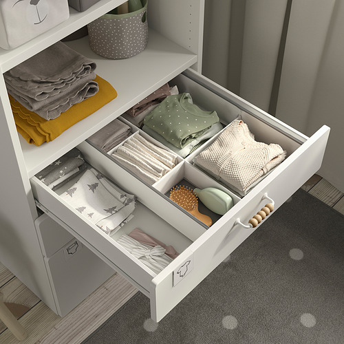 Cajón de la cómoda blanca organizado con espaciadores, que sostiene la ropa cuidadosamente doblada. Incluye un cepillo para el pelo y gomas para el pelo.