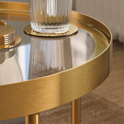 Elegante mesa auxiliar de metal dorado con tapa de cristal transparente, que muestra una artesanía refinada y un diseño de calidad.