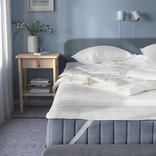 Dormitorio gris con cama hecha, cabecero gris claro, mesa auxiliar con vegetación y libros.
