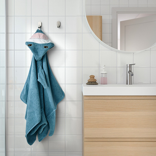 Una toalla de tiburón azul para niños cuelga en un baño, con una capucha con cabeza de tiburón, lazo para colgar, y es suave, absorbente y cálida.
