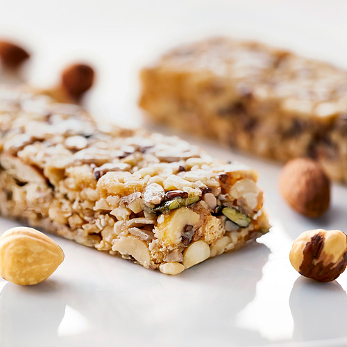 Barritas de cereales de nuez con almendras, avellanas y semillas visibles sobre una superficie blanca.