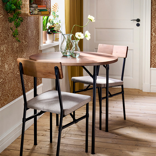 Pequeña mesa redonda de madera con patas de metal negro, sillas acolchadas grises. Decoración amplia y luminosa.