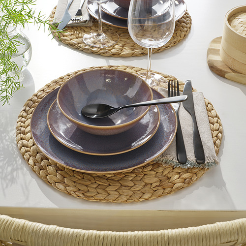 Mesa con mantel individual tejido, platos de cerámica, cuenco, cubiertos y copa de vino.