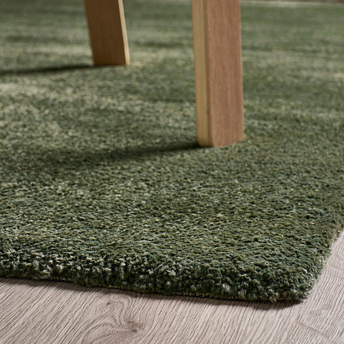 Alfombra verde y suave debajo de los muebles de madera que proporciona comodidad y amortiguación del sonido.