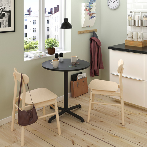 Pequeño y moderno juego de comedor con sillas de madera clara y mesa oscura, colocado cerca de una ventana en una acogedora cocina.