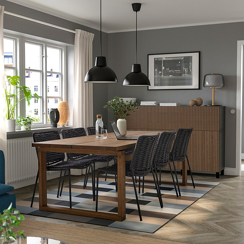 Comedor moderno con mesa de madera MÖRBYLÅNGA, sillas oscuras, bajo lámparas colgantes negras, paredes grises, cerca de una gran ventana con cortinas.