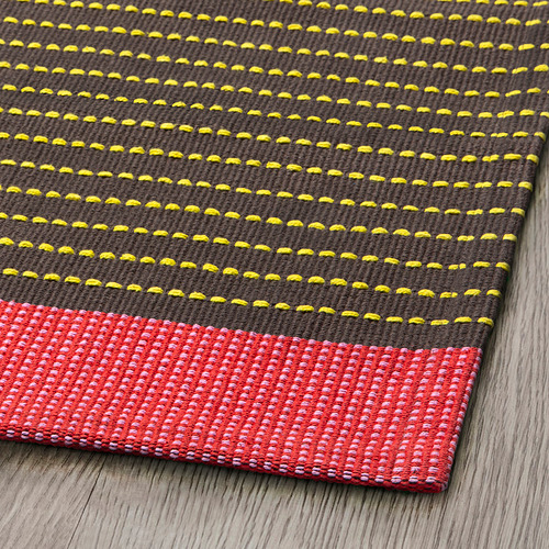 Alfombra de rayas coloridas con patrón amarillo y marrón, borde rojo sobre superficie de madera.