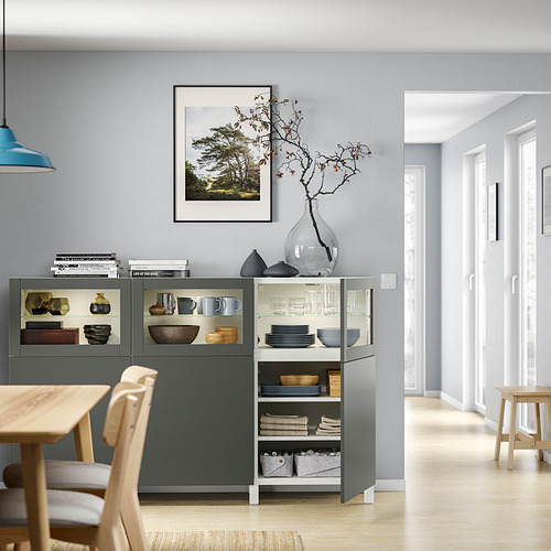 Comedor moderno con mueble de almacenamiento BESTÅ gris, mesa de madera, sillas y elementos decorativos.