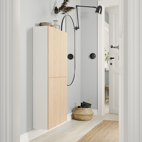 Pasillo moderno con mueble de almacenamiento BESTÅ blanco, puertas de madera natural, lámpara negra montada en la pared, cesta de mimbre, suelos de madera clara.