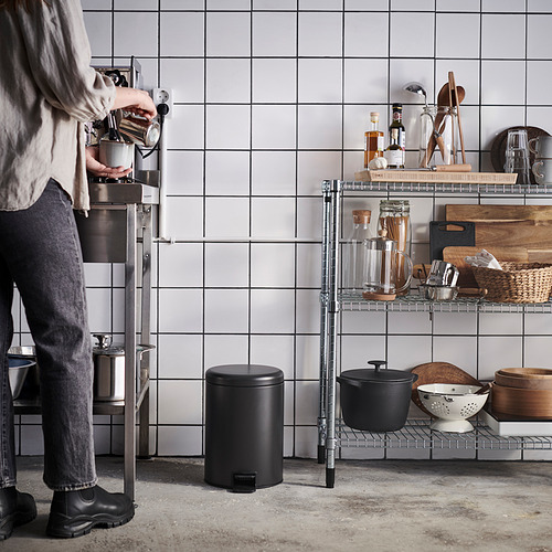 La persona sirve café junto a estantes metálicos organizados con utensilios de cocina.