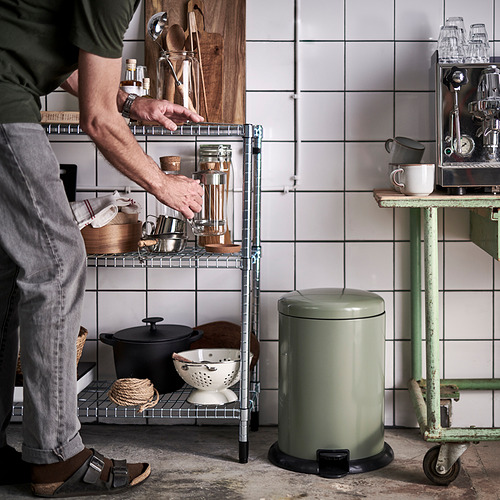 Hombre agarrando artículos de la estantería de la cocina con recipientes y utensilios de cocina. Papelera verde y cafetera cerca.