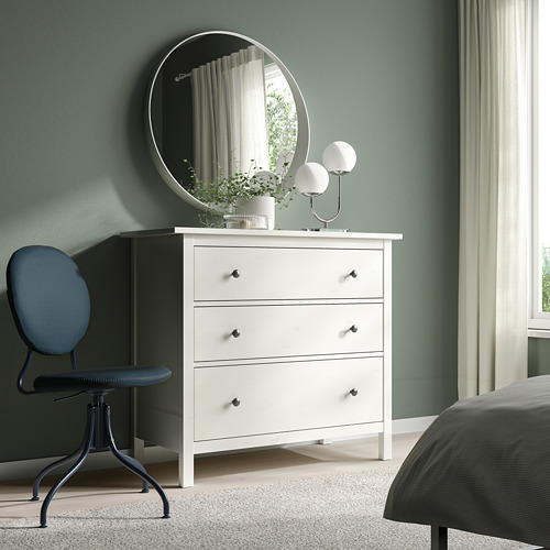 Dormitorio moderno con pared verde, tocador blanco, espejo redondo, silla giratoria azul, cama gris, lámparas blancas y planta en maceta.