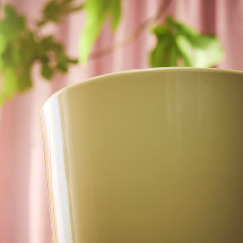 Primer plano de una maceta lisa y bien elaborada, de color amarillo claro, con fondo borroso en rosa y verde.