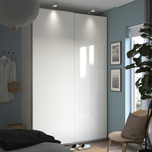 Dormitorio moderno con armario blanco PAX, paredes azules, ropa tendida, silla, planta y arte enmarcado.