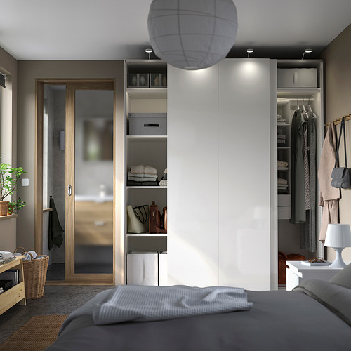 Dormitorio con armario PAX, blanco, diseño moderno, puertas correderas, estantería abierta con ropa, lámpara, y cama gris.