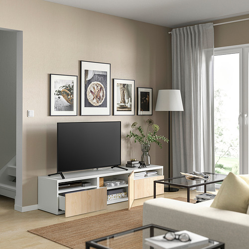 Moderno salón con banco de tv BESTÅ en blanco y roble. Televisor de pantalla plana, arte enmarcado, jarrón con vegetación y cortinas grises.