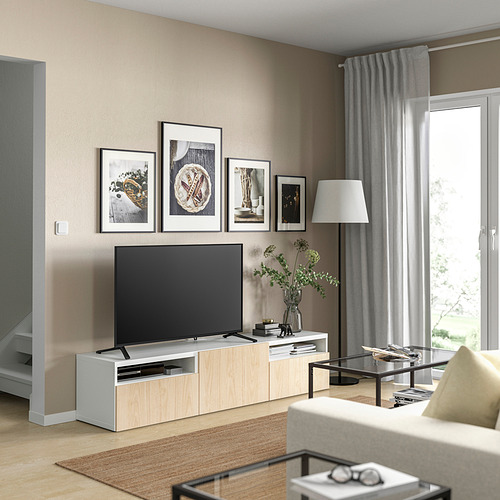 Sala de estar moderna con paredes beige, banco de tv BESTÅ blanco, tv, marcos decorativos, sofá beige, mesa de centro de vidrio y ventana con cortinas grises.