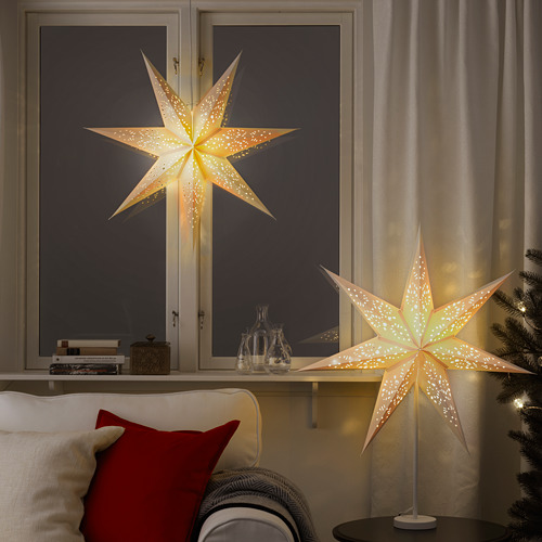 Acogedora sala de estar con dos pantallas iluminadas en forma de estrella, que crean un ambiente cálido, colocadas en el alféizar de la ventana y la mesa.