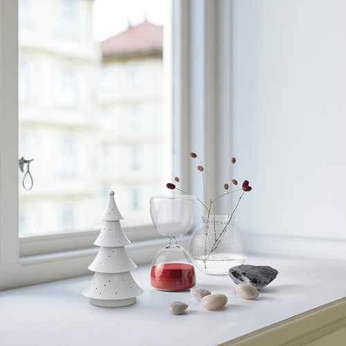 Pequeña lámpara blanca STRÅLA junto a una vela roja, jarrones transparentes y piedras junto a la ventana.