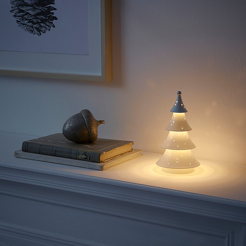 Una pequeña lámpara encendida en forma de árbol en una estantería, junto a libros y un objeto decorativo.