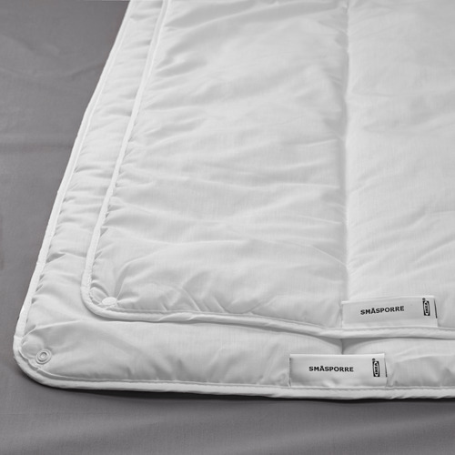 La imagen muestra un primer plano de un edredón blanco, cuidadosamente cosido, con sutiles etiquetas que dicen SMÅSPORRE e ikea.
