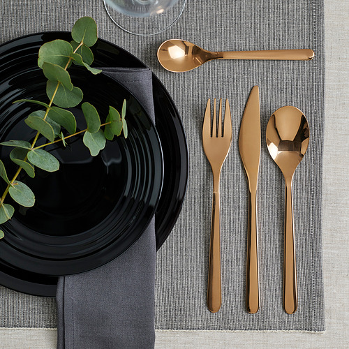 Elegante juego de cubiertos FÖRNUFT: mangos negros, oro brillante, acero inoxidable, diseño sencillo. Bien colocado sobre mantel gris, junto a plato y hojas negras.