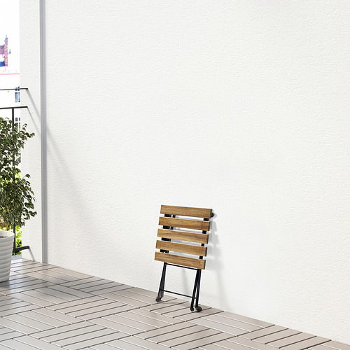 Taburete de madera plegado con ruedas, apoyado contra una pared blanca al aire libre.