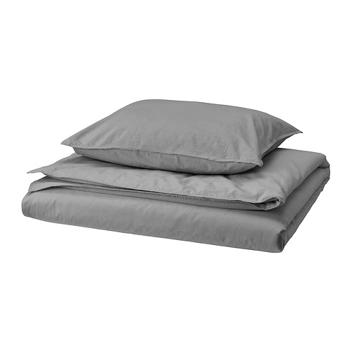 Un juego de funda nórdica y funda de almohada ÄNGSLILJA gris cuidadosamente doblado. La tela es de algodón lavado suave con un aspecto informal y relajado.
