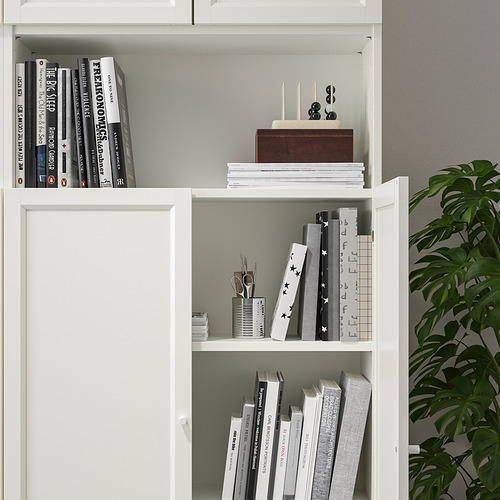 Estantería blanca con estantes ajustables, que sostienen libros y artículos decorativos. Una unidad de extensión de altura permite el máximo uso del espacio en la pared.