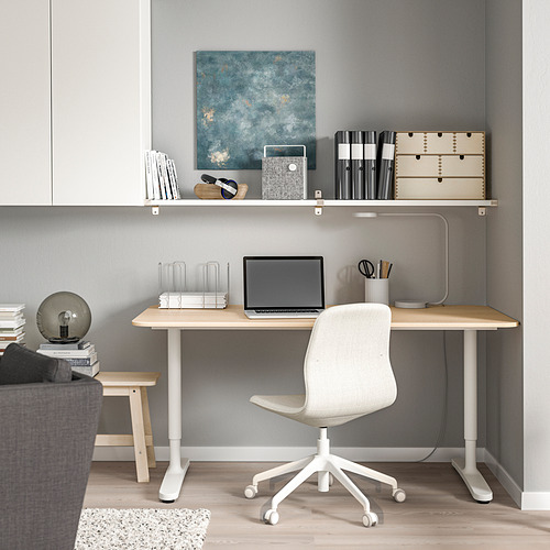 Moderna oficina en casa con escritorio de madera clara y silla blanca, computadora portátil, libros y estante de pared BERGSHULT arriba. Paredes grises.