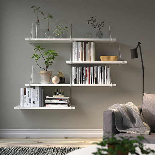 Salón moderno: estanterías blancas BERGSHULT con libros, jarrones, plantas. Pared gris, sofá, lámpara.